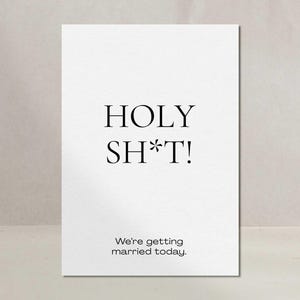 Könnte beinhalten: Eine weiße rechteckige Grußkarte mit schwarzem Text. Der obere Teil zeigt die Worte HOLY SH*T! in einer fetten Serifenschrift. Darunter steht in einer kleineren serifenlosen Schrift der Text We're getting married today. Die Karte ist schlicht.