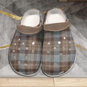 May include: A pair of plaid-patterned clogs. The clogs have a white interior, a brown strap, and a transparent exterior with a brown and blue plaid design. The shoes have multiple ventilation holes.