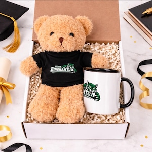 May include: A plush teddy bear wearing a black t-shirt with the text "SUNY BINGHAMTON" and a green logo, presented in a gift box with a matching mug. The mug is white with a black rim and handle, also featuring the university logo.