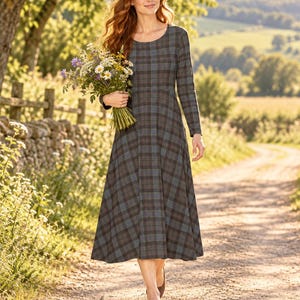 May include: A long-sleeved midi dress featuring a dark blue, brown, and grey plaid pattern with a round neckline and a fitted bodice that flares into a full skirt. The dress is worn with simple brown flat shoes and a bouquet of wildflowers.