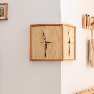 May include: A wooden clock with Roman numeral markings on the face. The clock is mounted on a corner of a white wall.