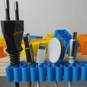 Può includere: Un organizzatore di cavi blu, flessibile e ondulato, sostiene cinque diversi cavi e connettori di ricarica, tra cui una spina elettrica nera a due poli, un connettore USB-A, un connettore Lightning, un caricabatterie magnetico circolare e un USB-C.