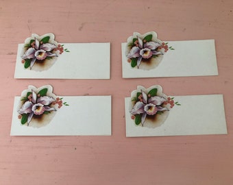 May include: Four white place cards with a pink orchid design. Each card has a blank space for writing a name.
