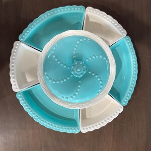 May include: A ceramic serving set with a central turquoise-colored, lidded dish surrounded by six pie-shaped plates. The plates alternate between turquoise and white, each with a beaded edge. The set is designed for serving appetizers or snacks.