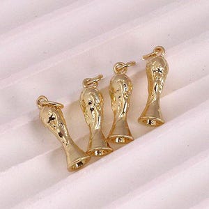 Puede incluir: Cinco abalorios de color dorado con forma de trofeo. Los abalorios son pequeños y detallados, con una superficie texturizada.