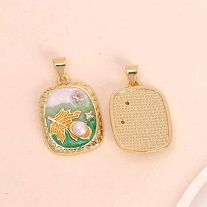 May include: Two gold-tone pendant charms. One charm features a green and white enamel design with a gold leaf and pearl. The other charm is plain and has a textured surface.