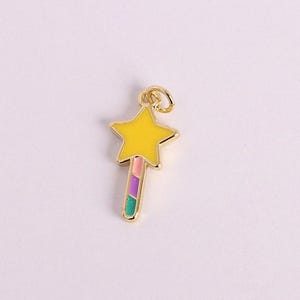 May include: A gold-colored star-shaped charm with a yellow center and a colorful striped wand. The charm has a small loop at the top for attaching to a necklace or bracelet. The wand has pink, purple, and green stripes.