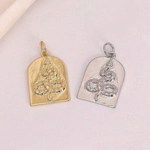 May include: Two pendant charms, one gold-toned and one silver-toned, each with a snake design inside a rectangular arch. The pendants have a textured surface and a small loop at the top for attaching to a chain or bracelet. Ideal for jewellery making.