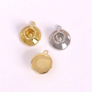 May include: Three small, metallic charms in gold and silver. Each charm has a circular base with a raised, cup-like centre and a small loop at the top for attachment. The charms are designed to resemble miniature teacups.