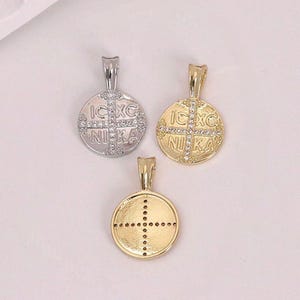 Op de afbeelding: Drie ronde hangers met een kruisontwerp. Eén is zilverkleurig, de andere twee zijn goudkleurig. De zilveren hanger en één gouden hanger hebben de tekst "IC XC NIKA" rond het kruis en zijn versierd met kleine kristallen. De derde gouden hanger heeft een gestippeld kruis.