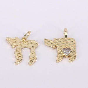 May include: Two gold-coloured pendants. One pendant is in the shape of the Hebrew letter "Chai", with decorative cutouts. The other pendant is in the shape of a tooth, with a heart-shaped gem. Both pendants have a small loop for a chain.