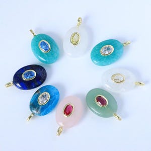 Può includere: Un assortimento di pendenti ovali in pietre preziose di vari colori, tra cui turchese, blu, bianco, rosa e verde. Ogni pendente presenta un'ansa dorata e una pietra centrale, come uno zaffiro o un rubino.