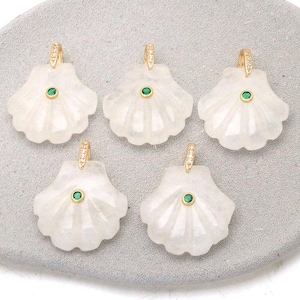 Op de afbeelding: Vijf schelpvormige hangers van doorschijnende witte steen, elk met een centrale ronde groene edelsteen gezet in goudkleurig metaal en een goudkleurig oogje aan de bovenkant versierd met kleine heldere steentjes voor bevestiging aan een ketting.