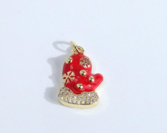 May include: A red enamel mitten charm with gold detailing and a base covered in small, clear crystals. The mitten has snowflake designs and hangs from a gold bail, suitable for jewellery making or festive crafts.