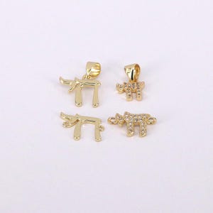 May include: Four gold-colored pendants in the shape of the Hebrew letter Chai. Two pendants are solid gold, while the other two are encrusted with small, clear gemstones. The pendants are displayed on a white background.
