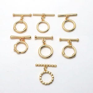 May include: A collection of seven gold-toned metal toggle clasps for jewellery making. Each piece consists of a circular ring and a matching T-bar connector. The designs vary, featuring smooth, ribbed, and beaded textures on the rings and bars.