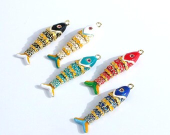 May include: Five colorful fish-shaped pendants with gold-tone accents. Each pendant features a different color scheme: black, white, teal, red, and blue, with intricate patterns and a small gemstone on the head. The pendants have a loop for attaching to a chain or other jewelry.