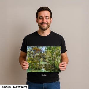 A man is holding a framed print of a forest scene, smiling and posing for the camera.