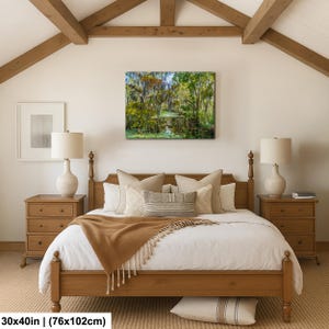a serene bedroom with a large bed, wooden furniture, and a painting of a forest scene hanging on the wall.