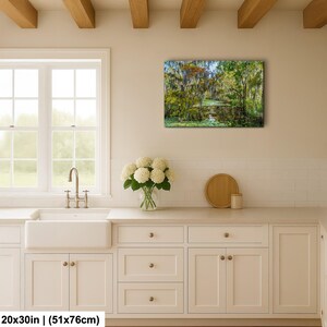 a serene kitchen scene with a large window overlooking a lush forest, a vase of white flowers on the counter, and a framed landscape painting hanging on the wall.