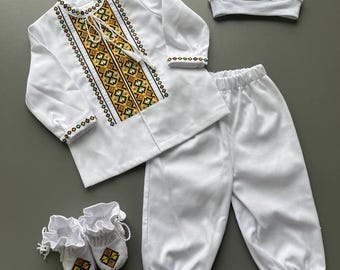 Puede incluir: Conjunto de ropa de bebé blanco con camisa de manga larga, pantalón, gorro y patucos. La camisa y el gorro tienen detalles bordados en amarillo, verde y marrón. Los patucos también tienen detalles bordados.
