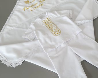 Könnte beinhalten: Ein weißes Set bestehend aus einem kurzärmeligen Hemd und einer Hose mit Spitzenbesatz, dazu eine passende weiße Decke mit Spitzenkanten und einer goldenen Stickerei mit der Aufschrift Theodore Jon Cormier.