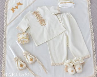 Puede incluir: Un conjunto de bautizo blanco con bordados dorados. El conjunto incluye un vestido, pantalones, un gorro, una almohada, dos velas y una manta. La manta tiene un borde de encaje y el texto "Baptism Studio Made in UA" está impreso en la parte inferior.