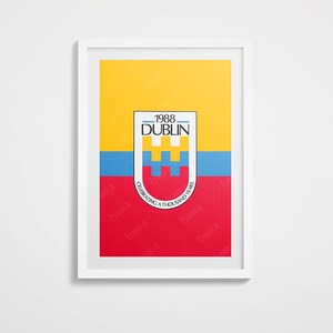 Op de afbeelding: Een ingelijste kunstafdruk met een kleurrijk ontwerp met gele, blauwe en rode secties. De print bevat de tekst "1988 DUBLIN" en "CELEBRATING A THOUSAND YEARS". Het kunstwerk is ingelijst in een witte lijst.