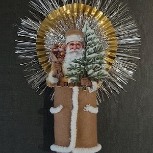 May include: A vintage Christmas ornament featuring a Santa Claus figure holding a small tree and a bag of gifts. The ornament is made of paper and fabric and is decorated with a gold and silver tinsel halo.