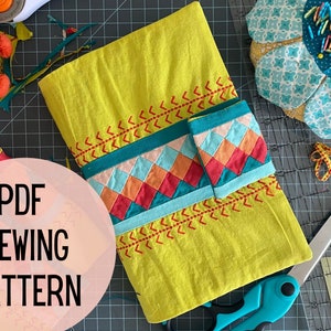 May include: A PDF sewing pattern for a yellow fabric pouch with a colourful patchwork design and red stitching. The pouch has a smaller pocket on the front. The image also shows a pincushion, scissors, and fabric scraps.