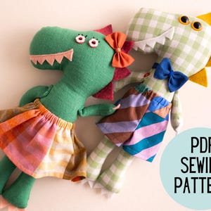 May include: Two handmade dinosaur plush toys. One is green with a pink and orange skirt and a red bow. The other is green and white checkered with a blue bow and a patchwork skirt. The toys have felt teeth and yellow accents. The image includes the text "PDF SEWING PATTERN".