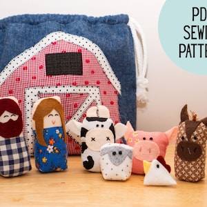 Può includere: Un set di piccole figure in tessuto tra cui due persone, una mucca, una pecora, un maiale, un pollo e un asino, davanti a una borsa con coulisse in denim blu con un'applicazione di fienile a quadri rossi e bianchi e il testo PDF SEWING PATTERN.