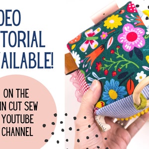 May include: A colorful fabric toy with a wooden ring, flowers, and a butterfly pattern. The toy is held in a hand and the text "VIDEO TUTORIAL AVAILABLE! ON THE PIN CUT SEW YOUTUBE CHANNEL" is visible in the background.