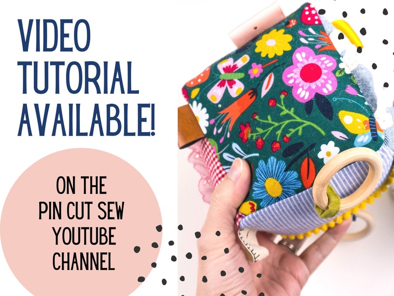 May include: A colorful fabric toy with a wooden ring, flowers, and a butterfly pattern. The toy is held in a hand and the text "VIDEO TUTORIAL AVAILABLE! ON THE PIN CUT SEW YOUTUBE CHANNEL" is visible in the background.