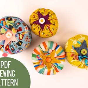May include: Four round fabric pincushions in various patterns including blue with mushroom motifs, yellow with floral prints, and multi-colored stripes. Each features a central felt star and button detail. Text reads PDF SEWING PATTERN.
