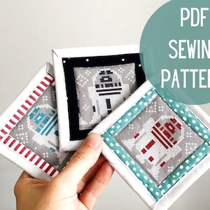 May include: Three different fabric coasters with a white background and a pixelated image of R2-D2 in the center. The coasters are framed with different colored fabric borders: red and white stripes, black, and teal with white polka dots. The text "PDF SEWING PATTERN" is in a teal circle in the upper right corner of the image.