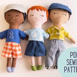 May include: Three handmade fabric dolls wearing different outfits. One doll has a blue shirt with the number 1, orange plaid shorts, and a gray cap. Another doll has a light blue shirt with a bird pattern and denim shorts. The third doll wears a yellow shirt and gray pants. The text "PDF SEWING PATTERN" is visible.