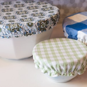 May include: Three reusable food covers in different patterns. The largest cover is blue and white with a floral design. The medium cover is green and white gingham. The smallest cover is blue and white gingham.