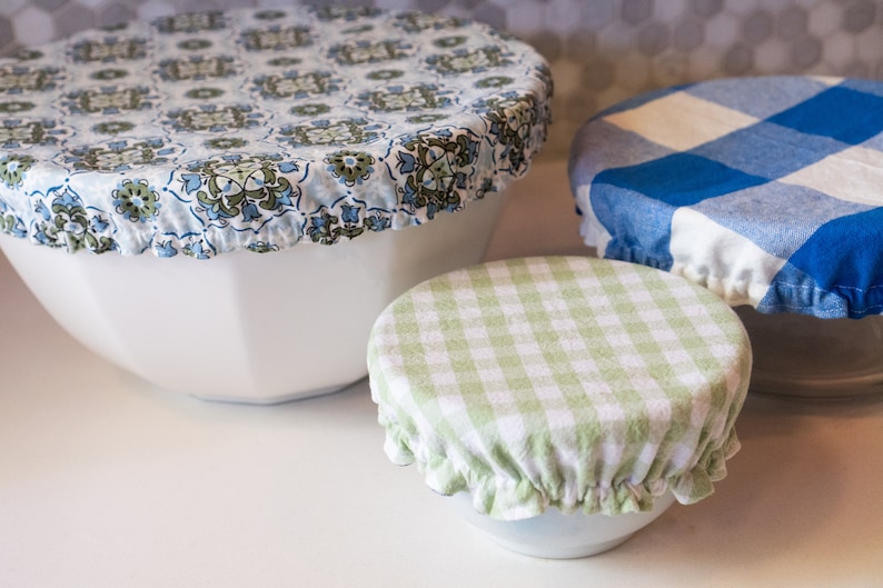 May include: Three reusable food covers in different patterns. The largest cover is blue and white with a floral design. The medium cover is green and white gingham. The smallest cover is blue and white gingham.