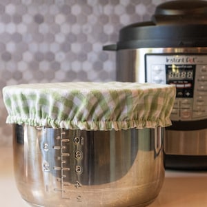 May include: A stainless steel Instant Pot with a green and white checkered fabric cover on top of the inner pot. The Instant Pot has a digital display showing "03:88".