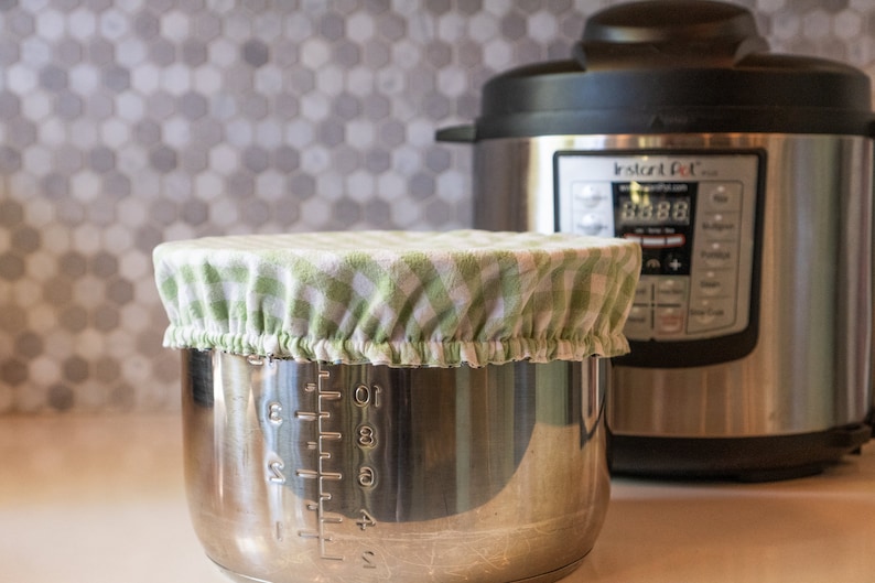 May include: A stainless steel Instant Pot with a green and white checkered fabric cover on top of the inner pot. The Instant Pot has a digital display showing "03:88".