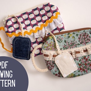 May include: Two fabric pouches with zipper closures, one with a purple floral pattern and the other with a floral pattern on a light blue background. Each pouch has a decorative tag and a handle. The text "PDF SEWING PATTERN" is in a dark blue circle.