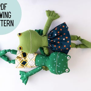 May include: Three green frog plushies with different patterns. One frog is wearing a yellow and black plaid skirt, another is wearing a blue and white polka dot skirt, and the third frog is wearing a green and white polka dot skirt.