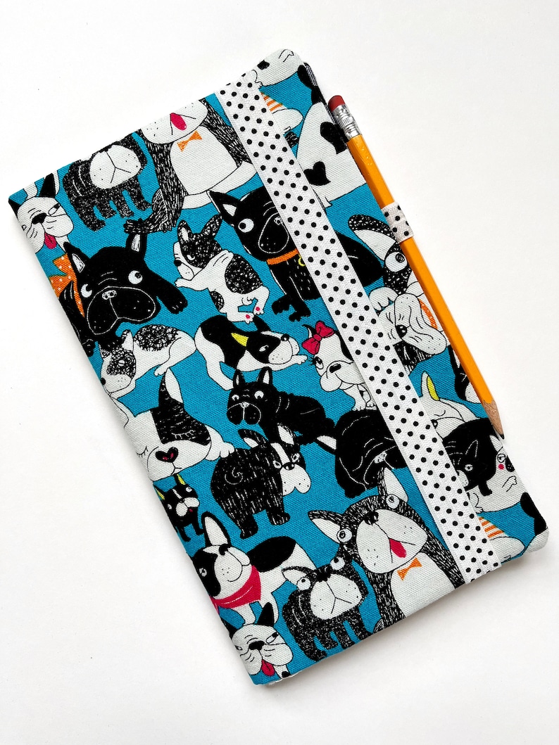 May include: A blue fabric pencil case with a black and white polka dot ribbon closure. The case is covered in a pattern of black and white cartoon French Bulldogs.