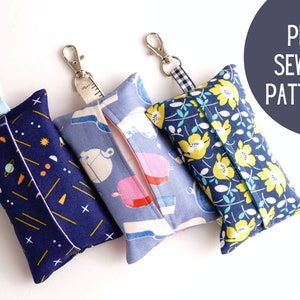May include: Three fabric tissue holders with different patterns. The first is navy blue with yellow and orange geometric shapes. The second is blue with a white and pink floral pattern. The third is navy blue with a yellow floral pattern. Each holder has a loop for attaching a key chain.
