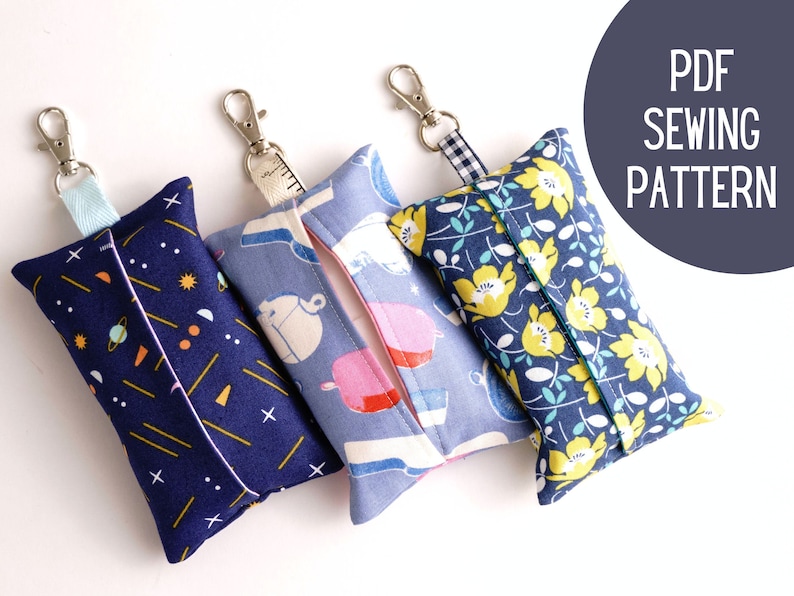 Pode incluir: Tr&ecirc;s porta-len&ccedil;os de tecido com padr&otilde;es diferentes. O primeiro &eacute; azul marinho com formas geom&eacute;tricas amarelas e laranja. O segundo &eacute; azul com um padr&atilde;o floral branco e rosa. O terceiro &eacute; azul marinho com um padr&atilde;o floral amarelo. Cada porta-len&ccedil;os tem um la&ccedil;o para prender um chaveiro.