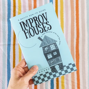 May include: A blue guide book titled "A Quilty How-To Guide Improv Houses" by Mikki Schreiner of Pin Cut Sew Studio. The cover features a black and white illustration of a house.