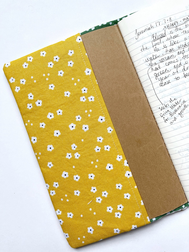 May include: A yellow fabric notebook cover with a white floral pattern. The cover is open to reveal a brown notebook with lined pages. The notebook has handwritten text on the pages, including the Bible verse Jeremiah 17:7+8.