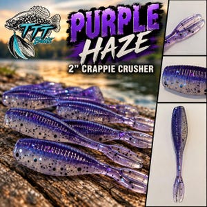 May include: A collection of 2-inch Purple Haze Crappie Crusher fishing lures. The soft plastic baits are translucent purple with black and blue glitter flakes, featuring a ribbed body and a split tail design, displayed on a wooden surface.
