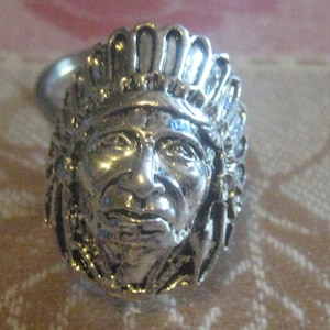 May include: A silver ring featuring a detailed depiction of a Native American chief wearing a headdress. The ring is a statement piece with intricate details.